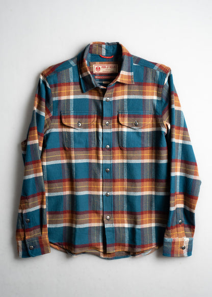 Plaid flannel shirt with blue, red, and yellow checks, featuring buttoned pockets, laid flat on a white background.