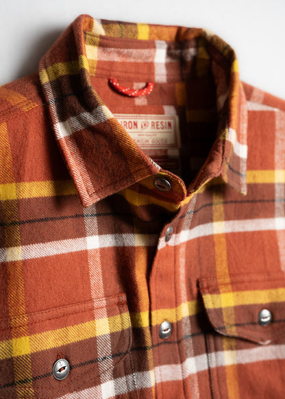 Close-up of an orange, yellow, and white plaid flannel shirt with metal buttons and a visible label inside the collar.