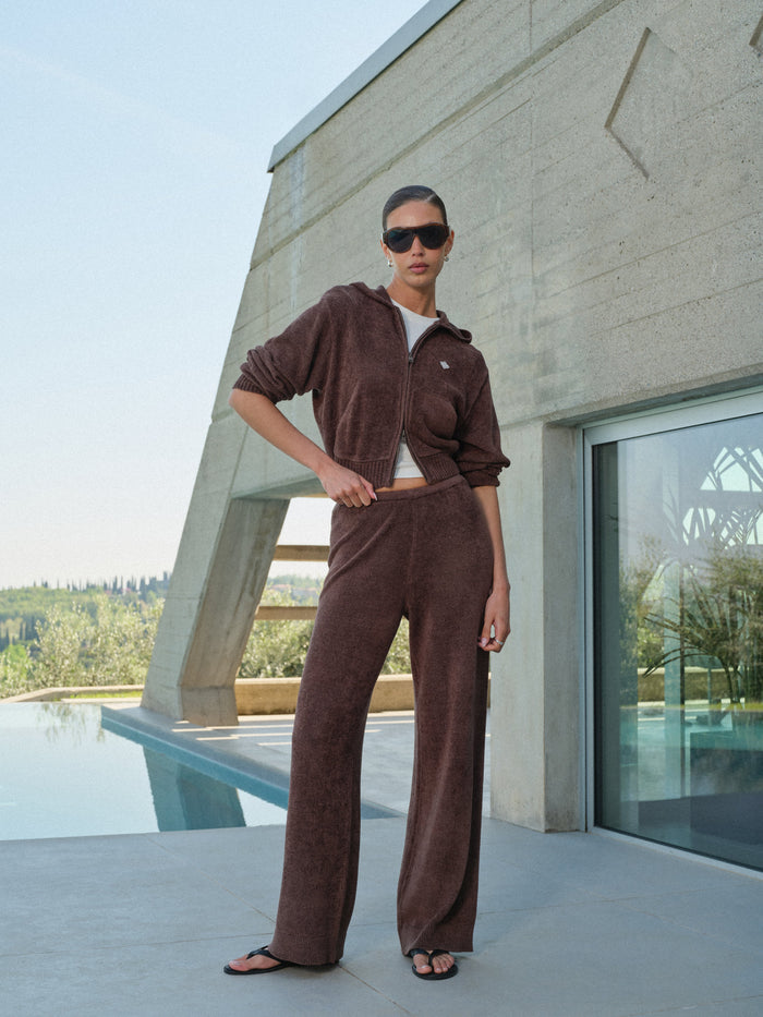 Person wearing a brown matching tracksuit standing in front of a modern building with a pool.